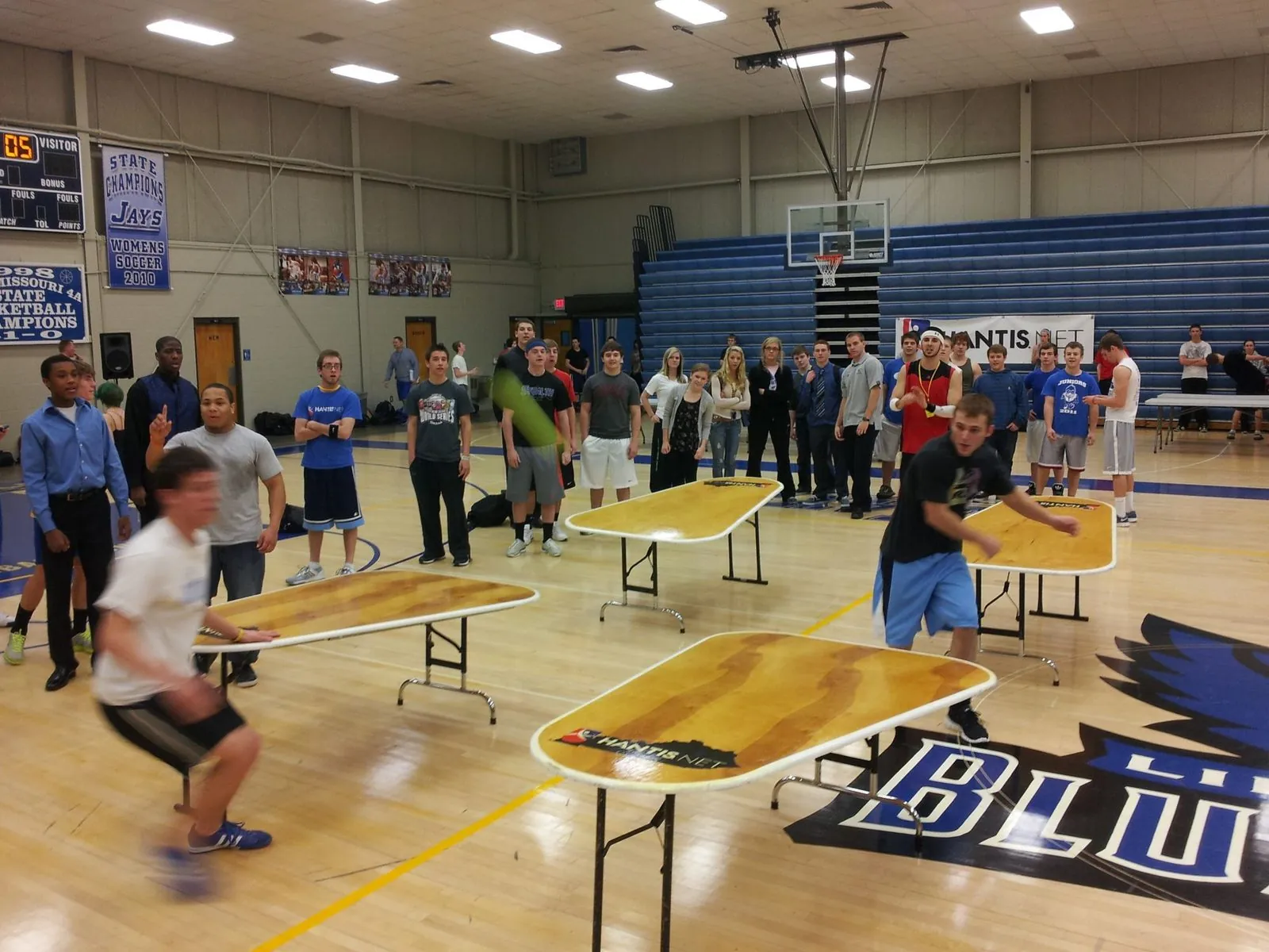 Students playing Hantis on four tables in a school gym while classmates watch